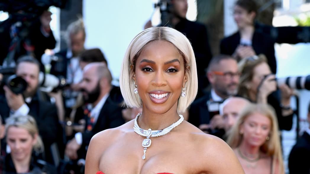 Singer and actor Kelly Rowland poses wearing a red strapless dress and silver necklace