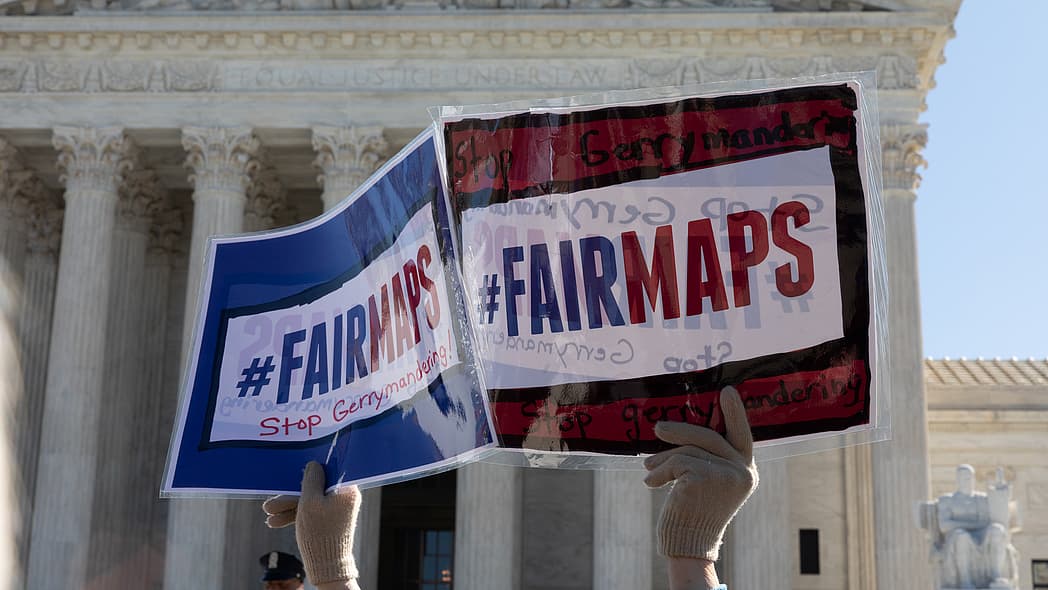 A set of hands holds up signs reading "#FairMaps - Stop Gerrymandering"
