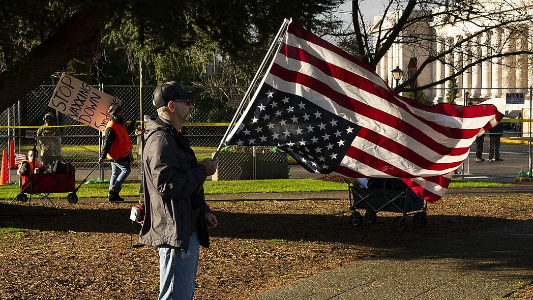 A conservative demonstrator holds a U.S. flag upside down as an anti-vaccination demonstrator walks nearby