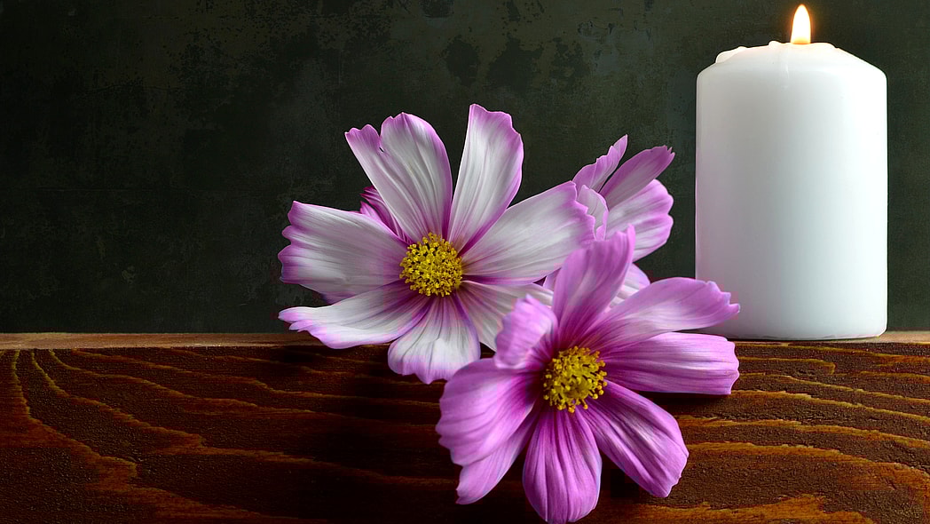 White burning candle and flowers thegrio.com