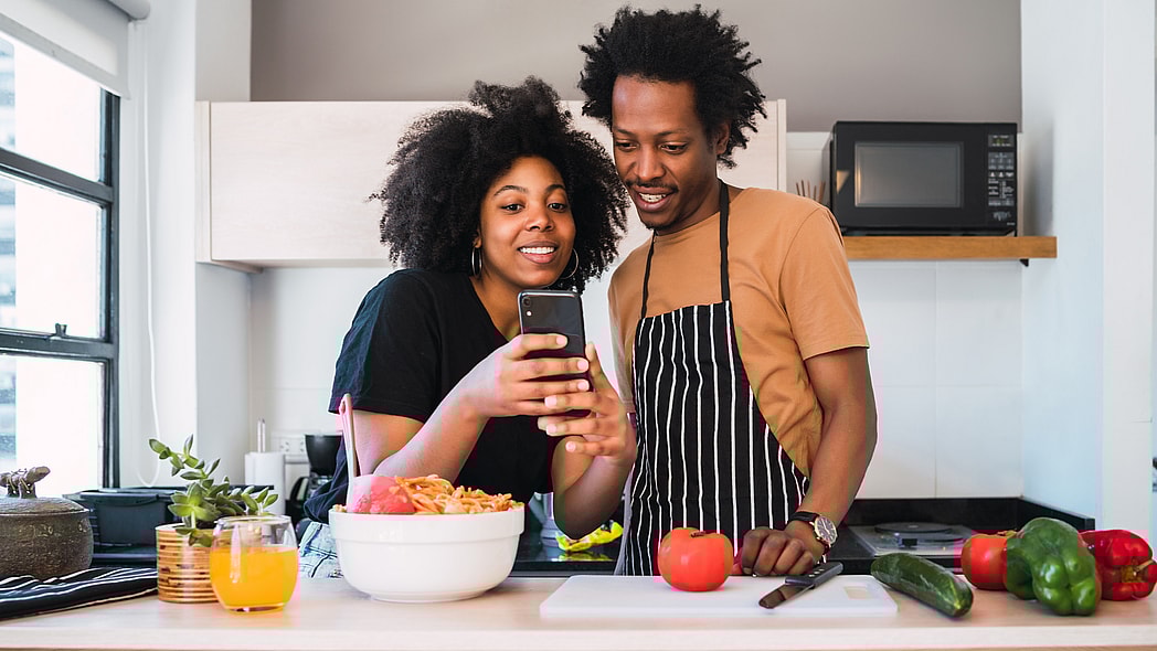 A young couple cooking together and using a mobile phone in the kitchen
