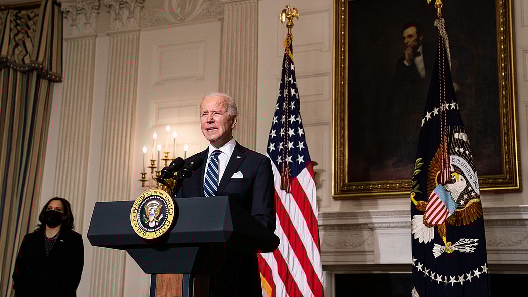 President Joe Biden stands behind a podium wearing a blue suit and blue striped tie