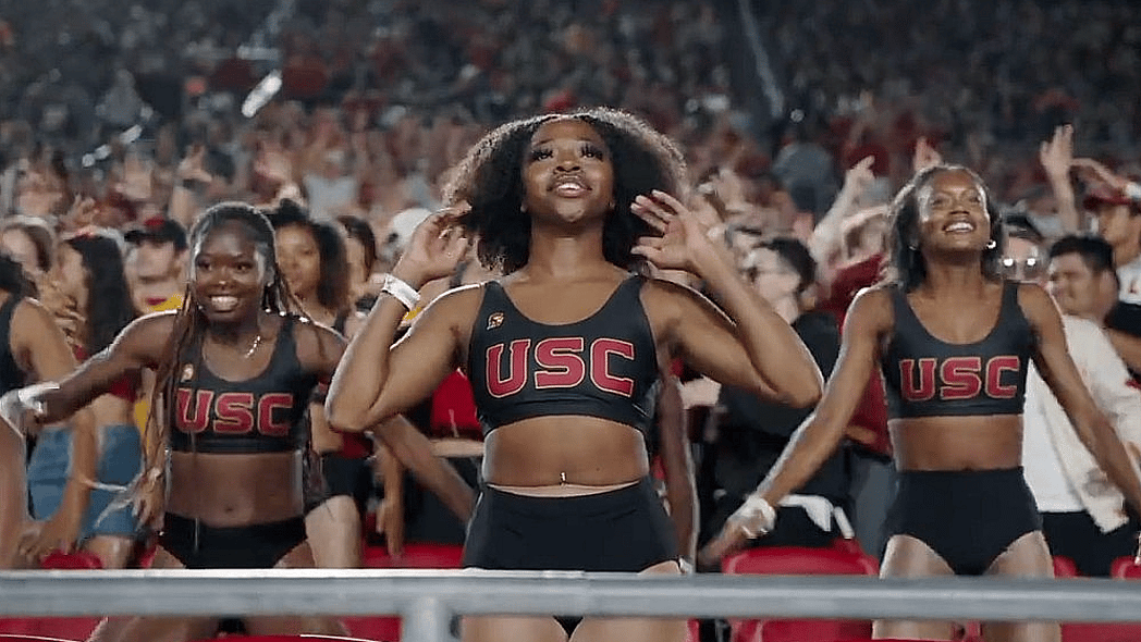 The Cardinal Divas perform in the stands at a sports game, wearing black two-piece outfits