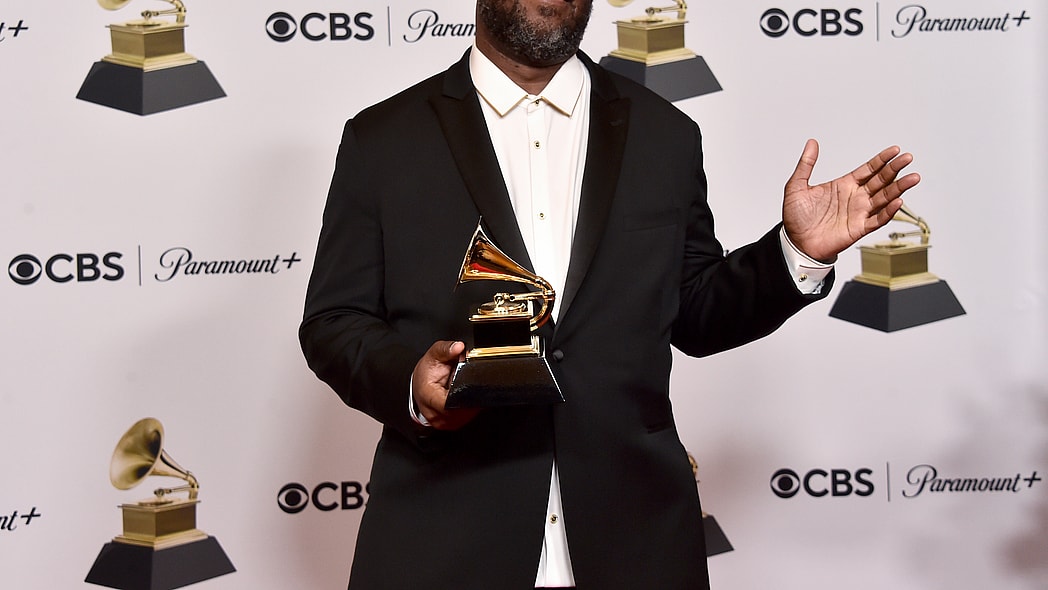 Rapper Robert Glasper holding his Grammy award, wearing a white shirt and black jacket