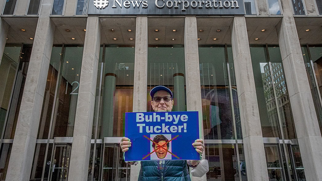 An activist holds a sign protesting Tucker Carlson outside the NewsCorp Building