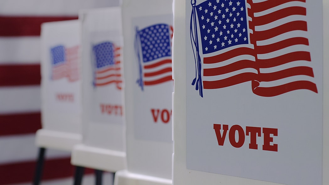 A row of voting machines with American flags and the word "Vote" on them