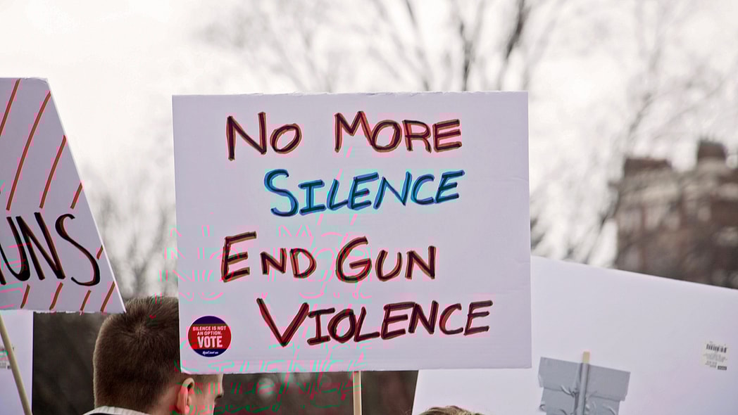 A protest sign reads "No more silence, End gun violence"