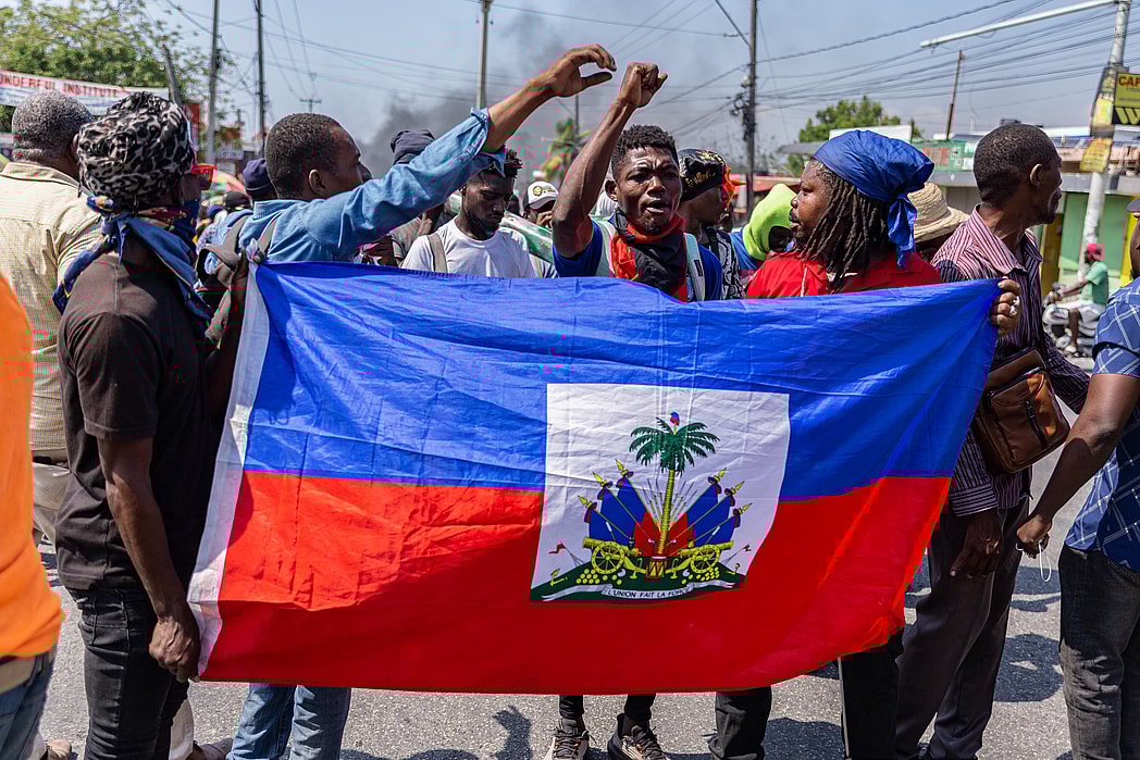 A group of people hold a Haitian flag and raise their hands in the air