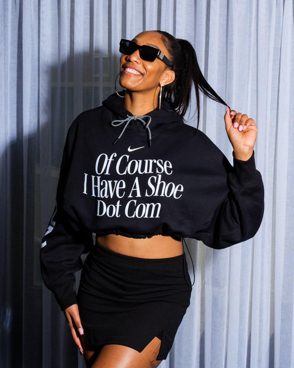 WNBA player A’ja Wilson holds a strand of her hair wearing sunglasses, a short black skirt and a black hoodie
