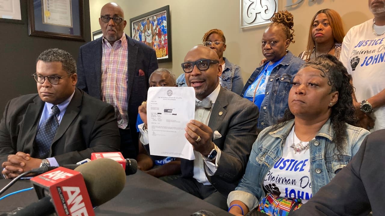 Lawyer Mawuli Davis holds up a document at a press conference surrounded by family members of Johnny Hollman Sr.