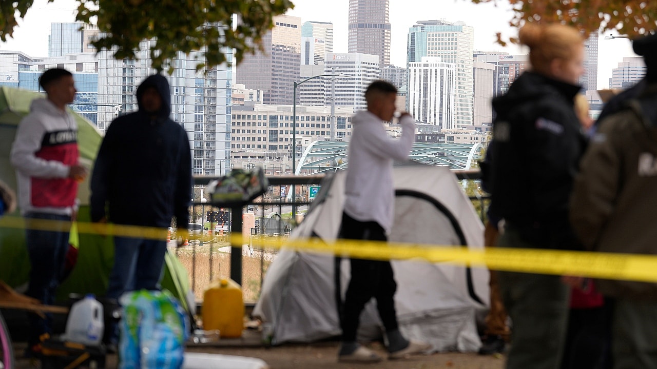 Occupants wait to see how police officers work during a city-sponsored sweep of a migrants’ encampment