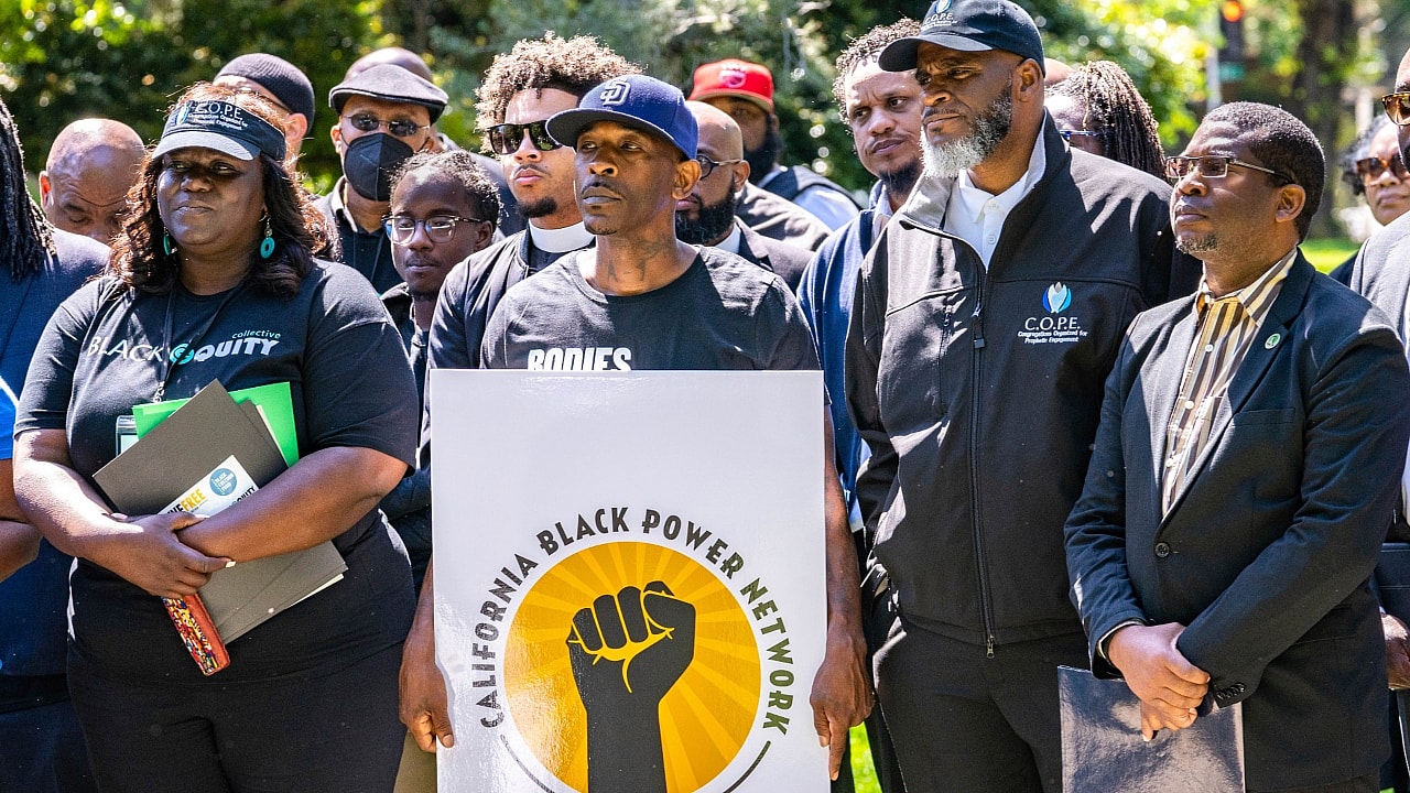 A group of people stands behind a sign reading "California Black Power Network" with a black fist on a gold background