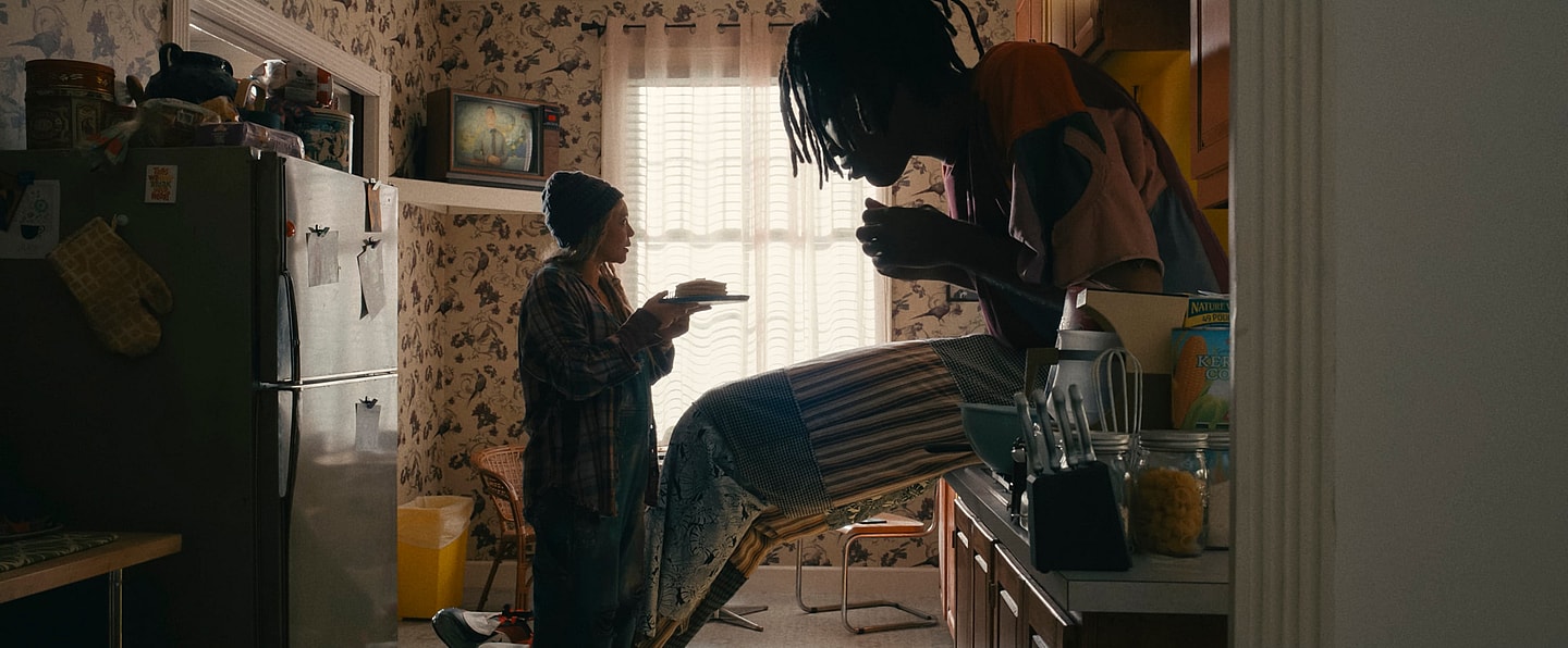 Actor Carmen Ejogo presents food on a plate to actor Jharrel Jerome as a giant
