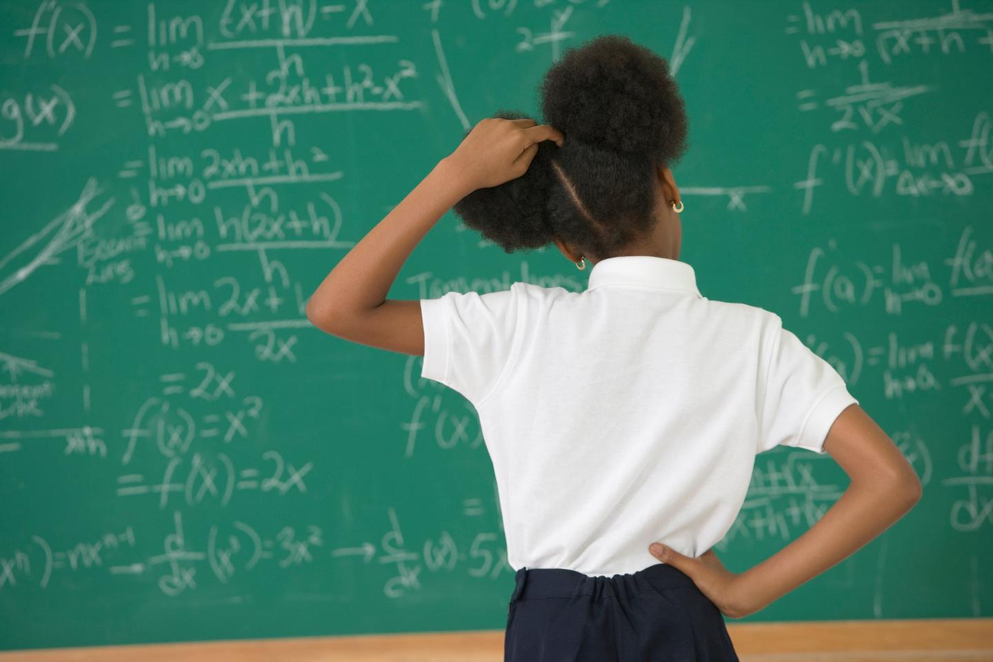 A girl stands at a chalkboard scratching her head