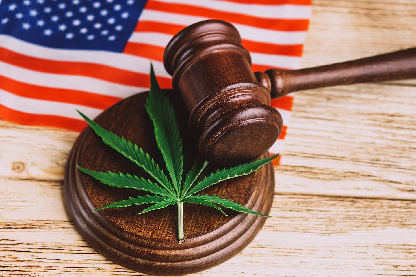 An American flag behind a gavel and a sound block with a marijuana leaf