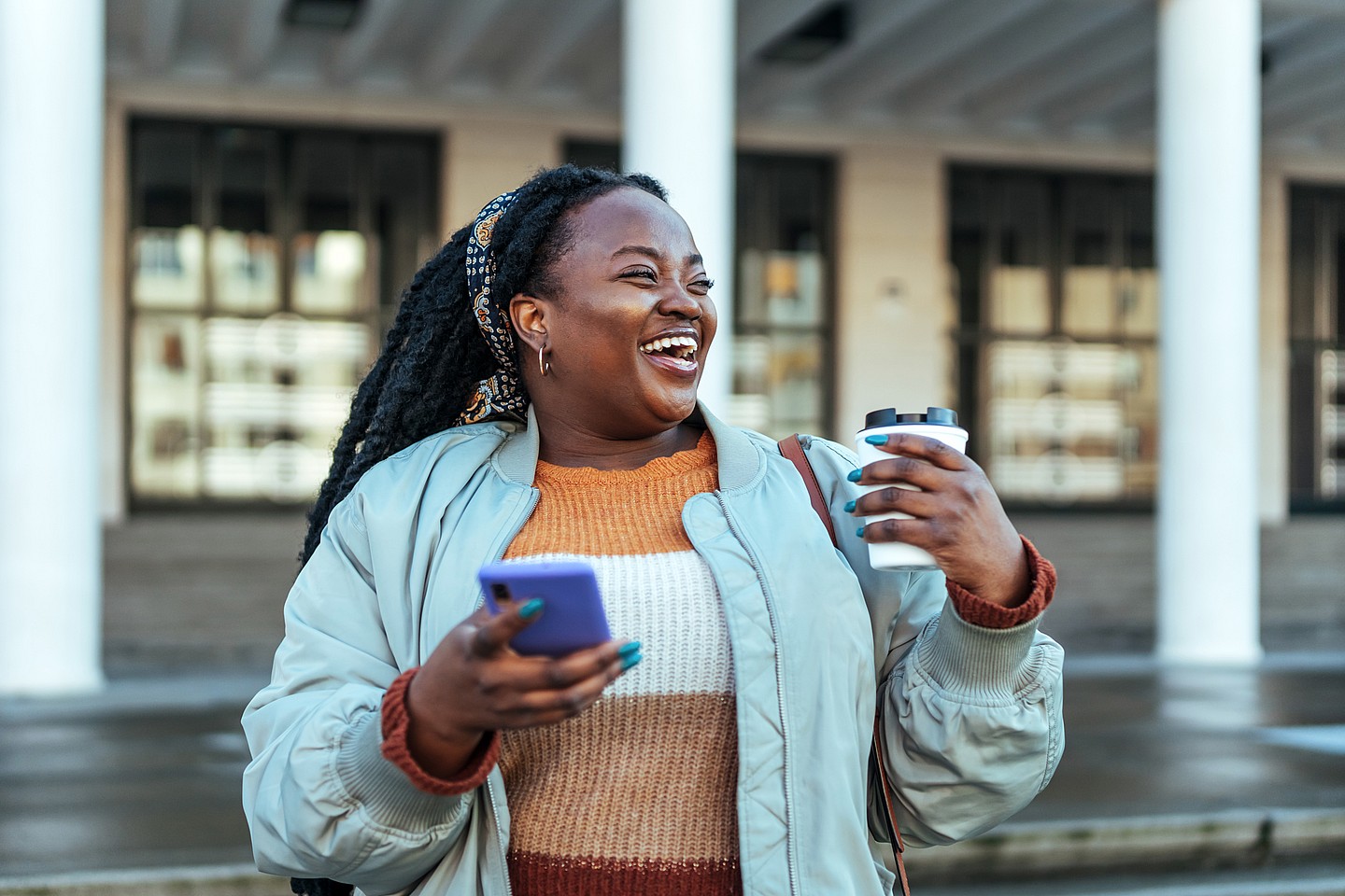 Woman laughing holding coffee and phone