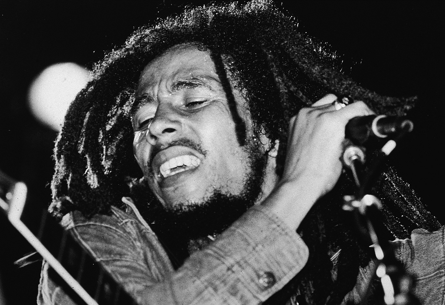 Black-and-white photo of the late Jamaican reggae musician Bob Marley on stage with a microphone in the late 1970s.