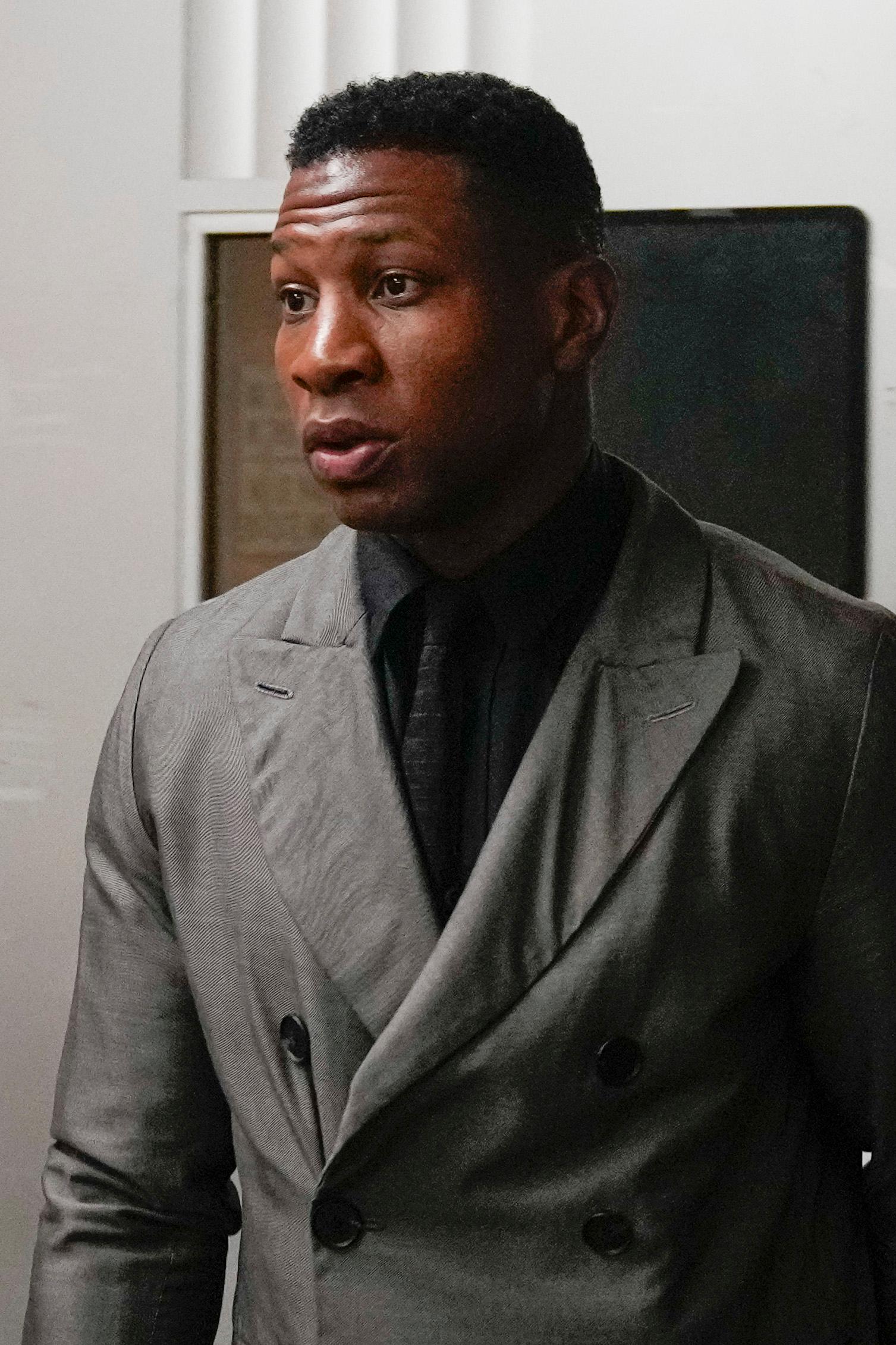 Actor Jonathan Majors wearing a gray coat and black shirt