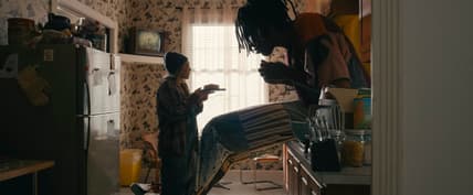 Actor Carmen Ejogo presents food on a plate to actor Jharrel Jerome as a giant