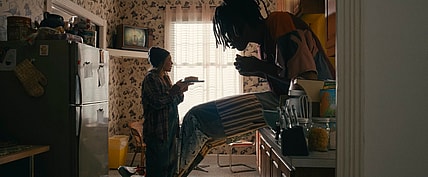 Actor Carmen Ejogo presents food on a plate to actor Jharrel Jerome as a giant