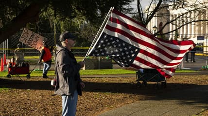 A conservative demonstrator holds a U.S. flag upside down as an anti-vaccination demonstrator walks nearby