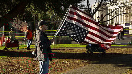 A conservative demonstrator holds a U.S. flag upside down as an anti-vaccination demonstrator walks nearby