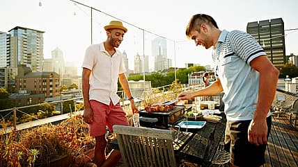 Two men cook shish kebabs on a tabletop grill