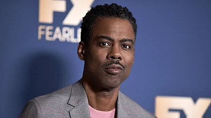 Actor and comedian Chris Rock wearing a gray checked jacket and pink shirt