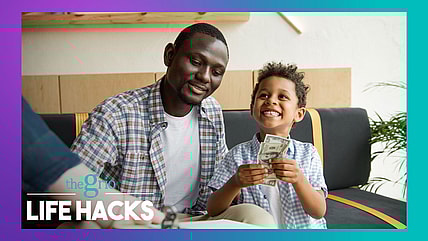 A man sits by a young boy holding $100 bills and smiling