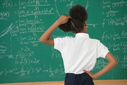 A girl stands at a chalkboard scratching her head