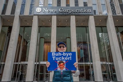 An activist holds a sign protesting Tucker Carlson outside the NewsCorp Building