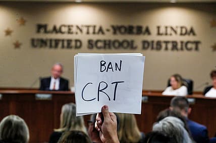 A hand holding a sign reading "Ban CRT"