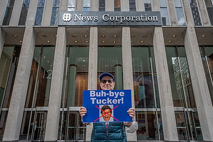 An activist holds a sign protesting Tucker Carlson outside the NewsCorp Building