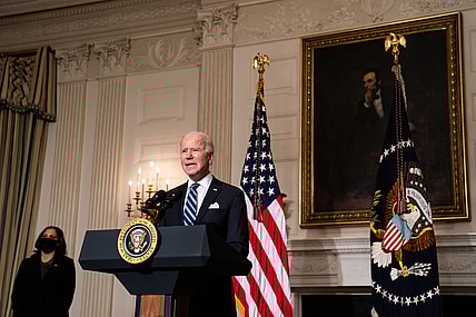 President Joe Biden stands behind a podium wearing a blue suit and blue striped tie