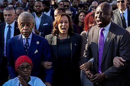 The Rev. Al Sharpton, Vice President Kamala Harris and Attorney Ben Crump walk and sing across the Edmund Pettus Bridge