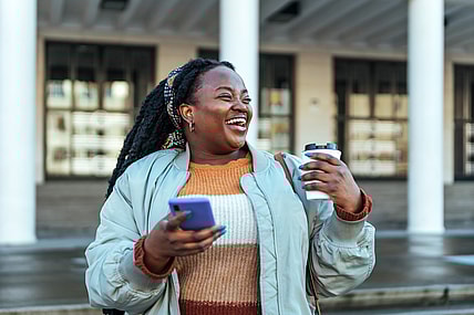 Woman laughing holding coffee and phone