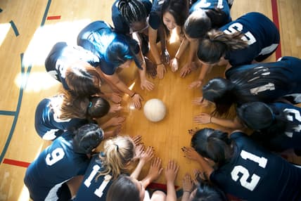Young people kneel on a basketball court around a volleyball