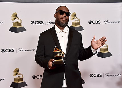 Rapper Robert Glasper holding his Grammy award, wearing a white shirt and black jacket