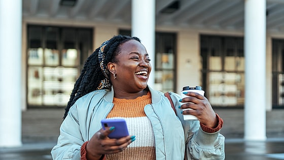Woman laughing holding coffee and phone