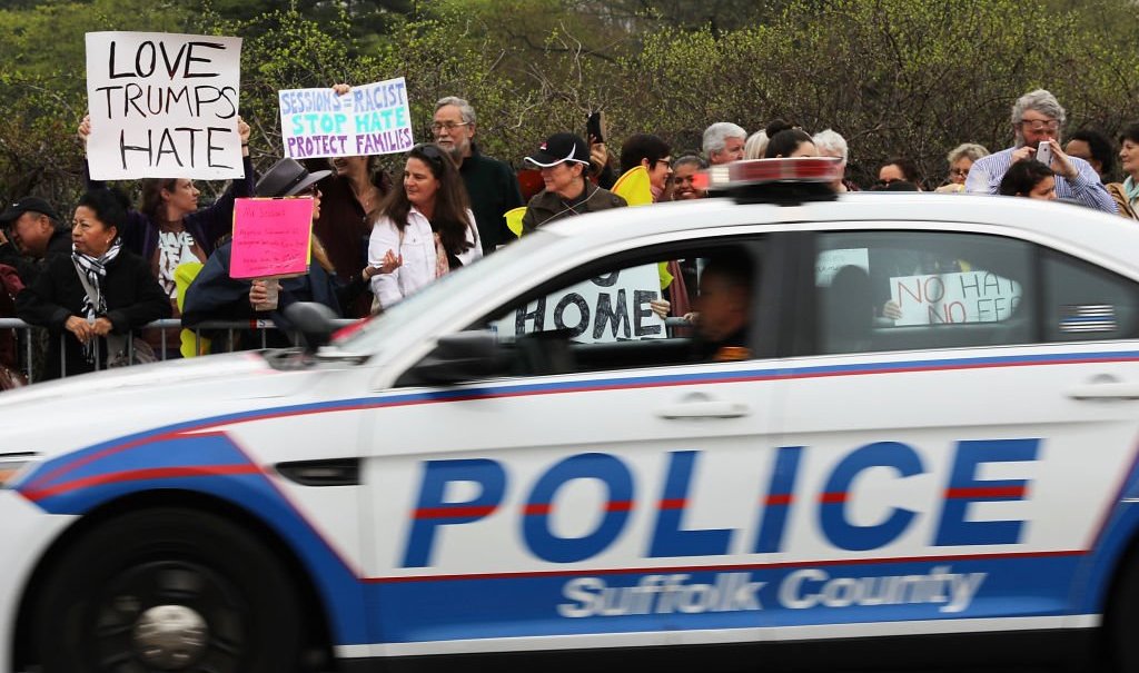 CENTRAL ISLIP, NY - APRIL 28: Police pass a group of protesters outside of the venue where Attorney General Jeff Sessions was to speak to local, state and federal law enforcement about a recent spate of gang related killings on April 28, 2017 in Central Islip, New York. Since the start of the school year the violent street gang MS-13 has been blamed for 11 deaths of mostly young people in residential Brentwood and neighboring Central Islip. The bodies have often been found in wooded areas and vacant lots. Sessions, who takes a tough stance on law and order, vowed to bring the gang leaders to justice. (Photo by Spencer Platt/Getty Images) thegrio.com