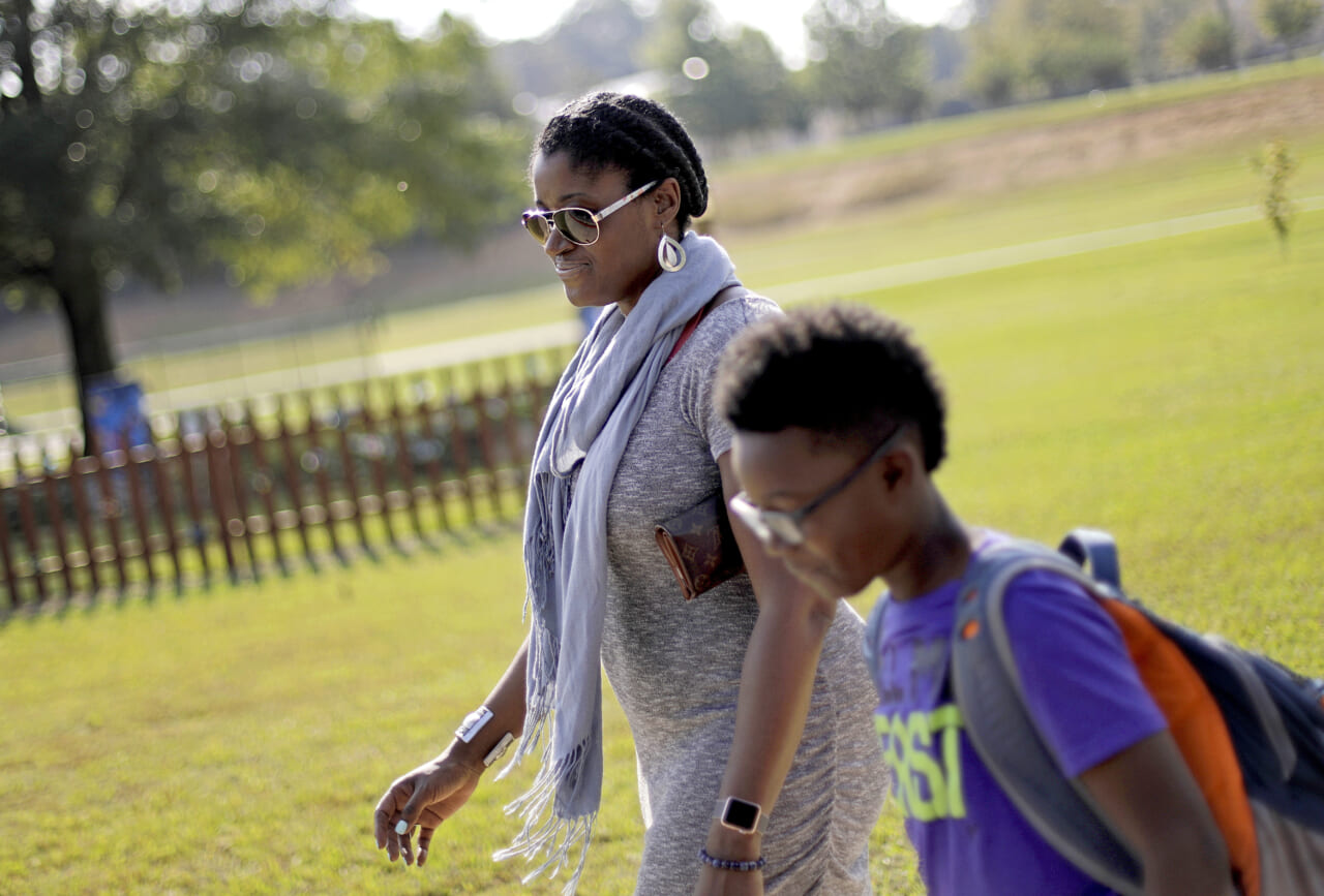 In this Oct. 11, 2017 file photo, Corrie Davis, left, picks up her son Turner from Big Shanty Elementary School in Kennesaw, Ga. The previous month, the school invited fifth-graders to dress up as characters from the Civil War. Davis says a white student dressed as a plantation owner approached her son and said "You are my slave." She requested that the school to stop the annual Civil War dress-up day. Recently, an investigation by New York Attorney General Letitia James found in May that a mock "slave auction" that singled out black students at the private Chapel School in Westchester County had a profoundly negative effect on all involved students. (AP Photo/David Goldman, File)