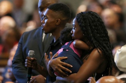 In this June 18, 2019 file photo Dravon Ames, holding microphone, speaks to Phoenix Police Chief Jeri Williams and Phoenix Mayor Kate Gallego, as his fiancee, Iesha Harper, right, holds 1-year-old daughter London, at a community meeting in Phoenix. Still stinging from national outrage sparked this summer by a videotaped encounter of officers pointing guns and cursing at the family, community members are holding low-key meetings aimed at helping Phoenix officials figure out how citizens could help oversee the city's officers. (AP Photo/Ross D. Franklin, File) thegrio.com
