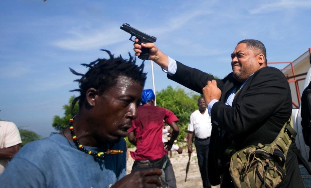 Ruling party Senator Ralph Fethiere fires his gun outside Parliament as he arrives for a ceremony to ratify Fritz William Michel's nomination as prime minister in Port-au-Prince, Haiti, Monday, Sept. 23, 2019. Opposition members confronted ruling-party senators, and Fethiere pulled a pistol when protesters rushed at him and members of his entourage. (AP Photo/Dieu Nalio Chery) thegrio.com