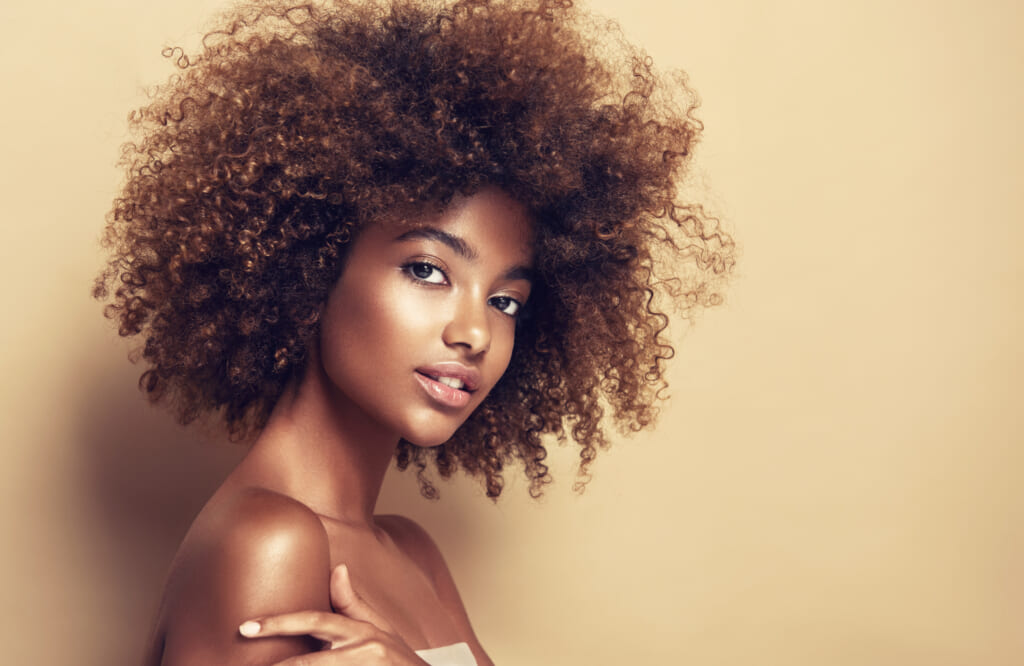 Beautiful black woman . Beauty portrait of african american woman with clean healthy skin on beige background. Smiling beautiful afro girl.Curly black hair thegrio.com