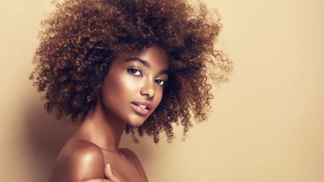 Beautiful black woman . Beauty portrait of african american woman with clean healthy skin on beige background. Smiling beautiful afro girl.Curly black hair thegrio.com