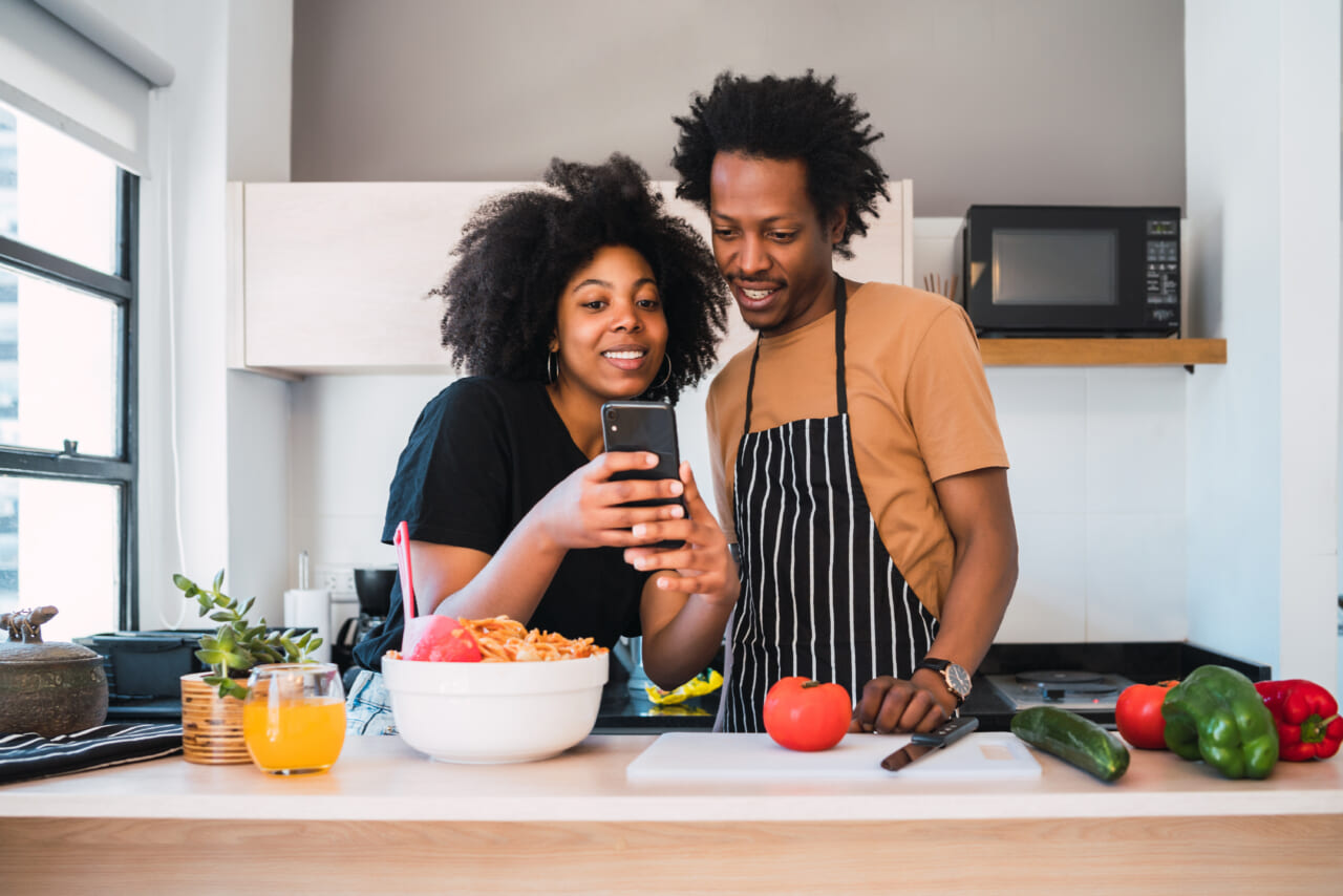 A young couple cooking together and using a mobile phone in the kitchen