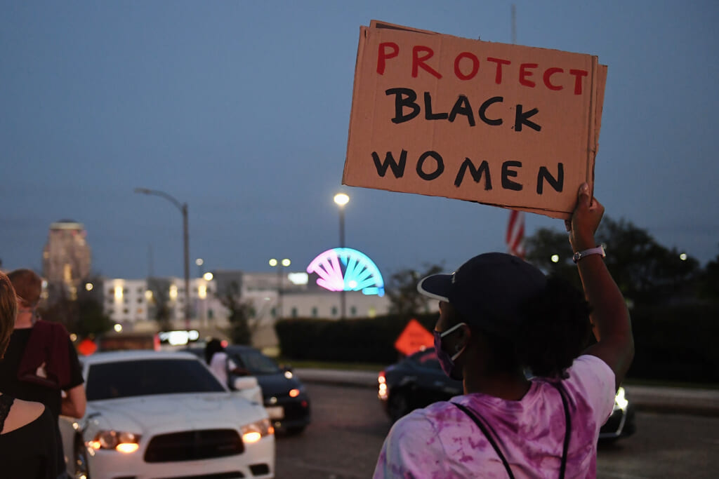 A woman holds a "Protect Black Women" sign.