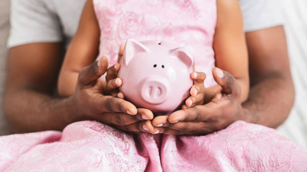 Black father and his daughter hold piggybank