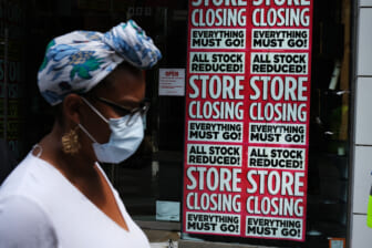 Black woman in front of "Store Closing" sign on business, theGrio.com