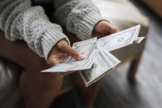 Black woman holds money, theGrio.com